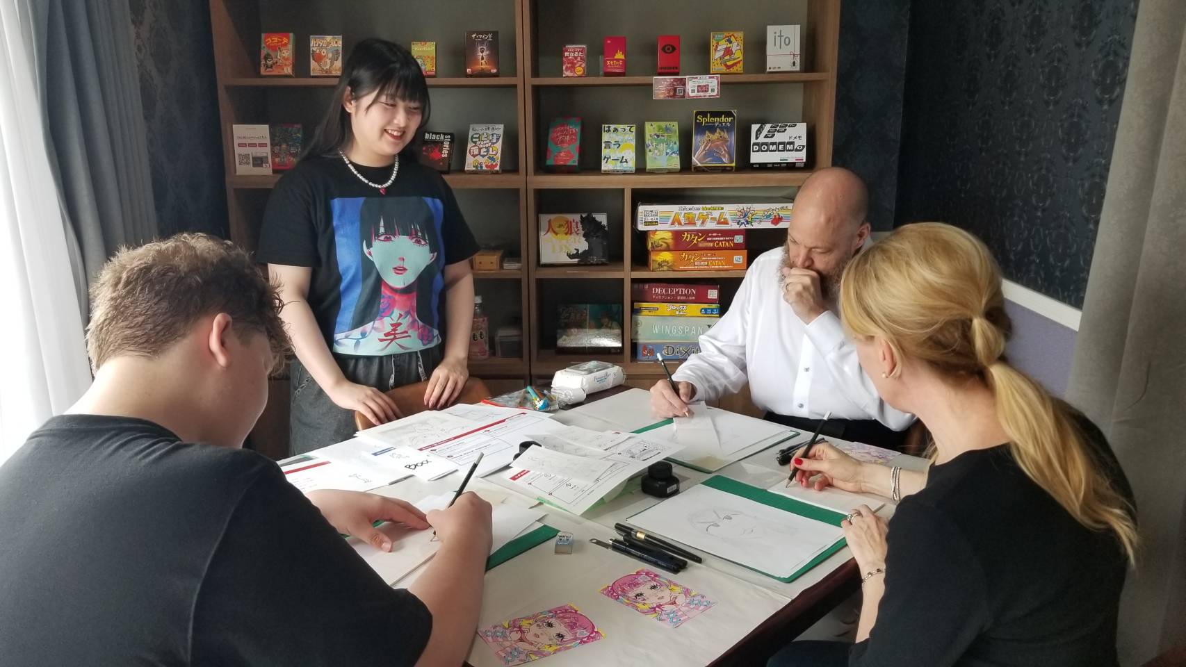 Guests gathered around the table sketching together, game shelf in the background