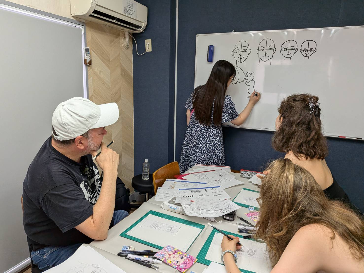 Sensei demonstrating character drawing on the whiteboard while guests watch